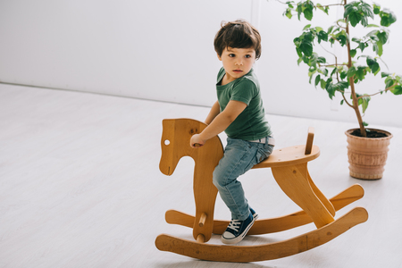 cute child sitting on wooden rocking horse in living roomの写真素材