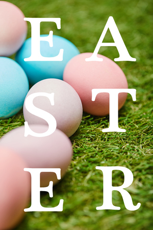 pile of multicolored painted chicken eggs with Easter lettering on green grass