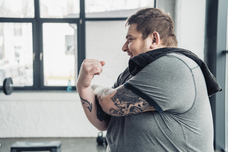 overweight tattooed man in white t-shirt smiling and stretching arms at sports centerの写真素材