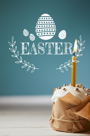 traditional Easter cake with burning candle on blue background with easter letteringの写真素材