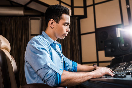 concentrated mixed race sound producer working at mixing console in recording studioの写真素材