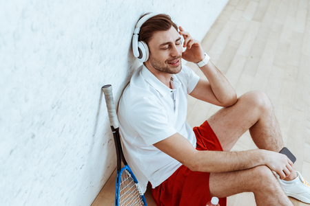 Smiling squash player sitting on floor and listening music in headphones with closed eyesの写真素材