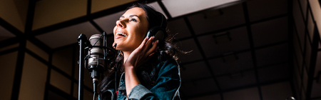 Panoramic shot of beautiful inspired woman singing near microphone in recording studioの写真素材