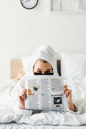 Woman in sunglasses, jewelry and with towel on head reading business newspaper in bedの写真素材