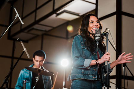 selective focus of excited woman singing in recording studio while handsome mixed race musician playing drumsの写真素材