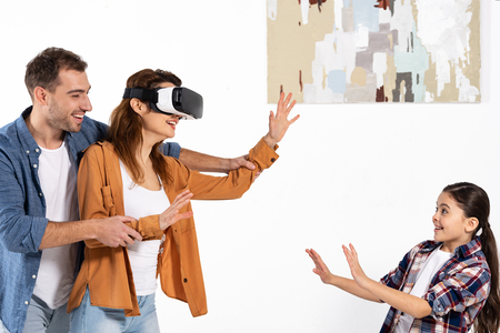 happy man holding hands of cheerful woman in virtual reality headset near daughterの写真素材