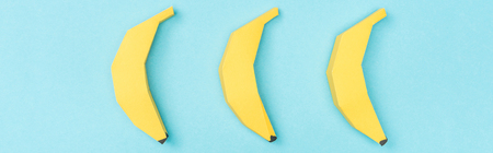 Panoramic shot of arranged yellow paper bananas isolated on blue backgroundの写真素材