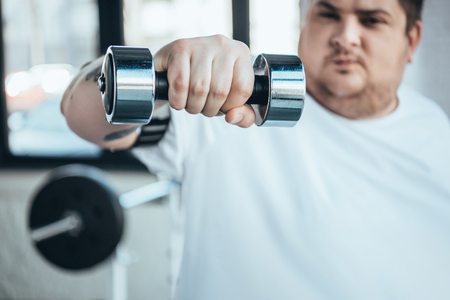 Cropped view of Overweight man looking at camera while training with dumbbell at gymの写真素材