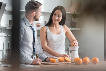 happy brunette girl squeezing orange and looking at bearded manの写真素材