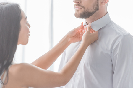 brunette woman touching collars of bearded man in white shirtの写真素材