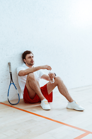 Squash player sitting on floor and holding bottle of waterの写真素材