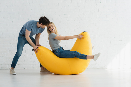 cheerful woman sitting on yellow bean bag chair and looking at handsome manの写真素材