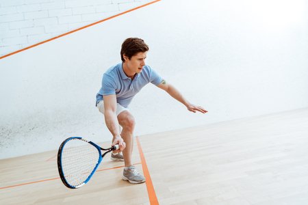 Emotional sportsman in blue polo shirt playing squash in four-walled courtの写真素材