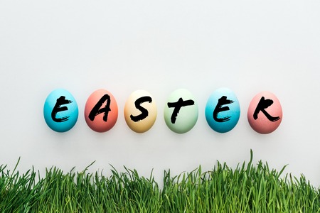 top view of painted chicken eggs with Easter word near green grass on grey backgroundの写真素材
