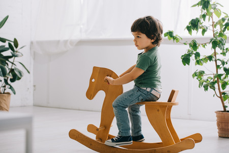 Child sitting on wooden rocking horse in living roomの写真素材
