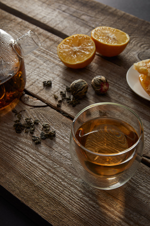 Transparent teapot with glass of Chinese blooming tea, tea balls and lemons on wooden tableの写真素材