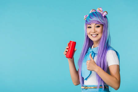 Smiling Asian anime girl in wig holding can with beverage isolated on blue backgroundの写真素材
