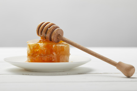 Plate with honey dripper and delicious honeycomb on white wooden table isolated on grey backgroundの写真素材