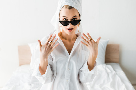 Shocked young stylish woman in shirt, sunglasses, jewelry and with towel on head looking at cameraの写真素材