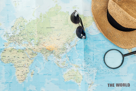 Top view of straw hat, sunglasses and magnifier on world mapの写真素材