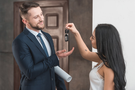 Happy brunette girlfriend giving key to handsome bearded manの写真素材