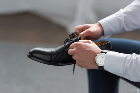 Cropped view of man with watch on hand holding black shoeの写真素材