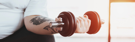 Panoramic shot of Overweight tattooed man training with dumbbell at gymの写真素材