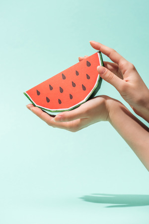 Cropped view of young woman holding paper watermelon with seeds on turquoise backgroundの写真素材