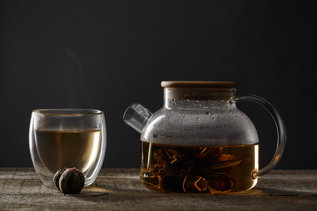 Transparent teapot and glass with blooming tea on wooden table isolated on black backgroundの写真素材
