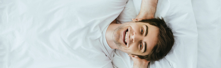 Panoramic shot of happy man looking at camera while lying on bedの写真素材