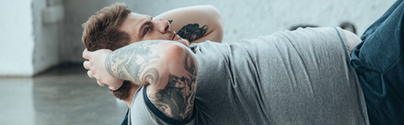 Panoramic shot of overweight tattooed man doing sit up exercise at sports centerの写真素材
