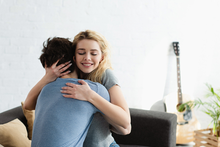 Happy young woman smiling while hugging boyfriend at homeの写真素材