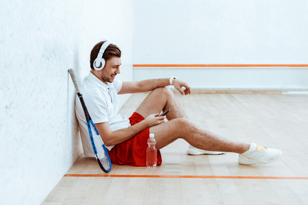 Smiling squash player listening music in headphones and using smartphoneの写真素材