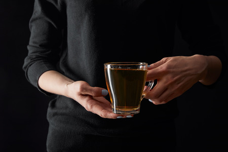 Cropped view of young woman holding transparent cup of green tea isolated on black backgroundの写真素材