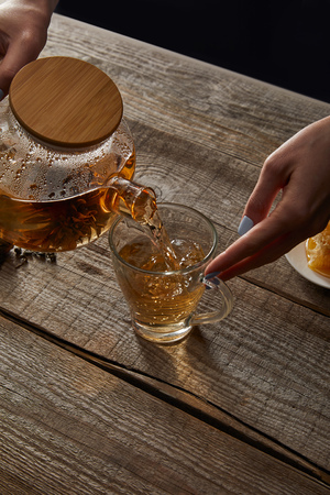 Cropped view of young woman pouring traditional Chinese blooming tea in cup on wooden tableの写真素材
