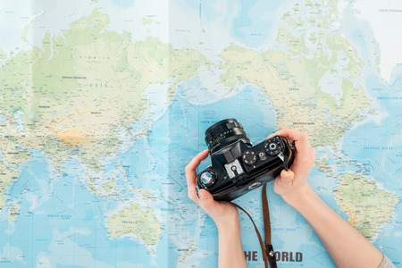 Cropped view of woman holding film camera on world mapの写真素材