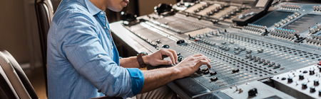 Panoramic shot of mixed race sound producer working at mixing console in recording studio