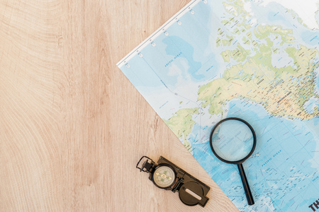 Top view of world map, magnifier and compass on wooden surface