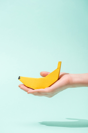 Cropped view of young woman holding paper banana on turquoise background with copy spaceの写真素材