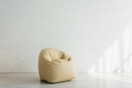 Sunlight near beige bean bag chair near brick wall in modern homeの写真素材