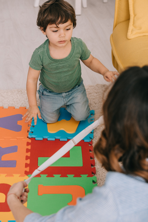 Cropped view of mother and son with alphabet puzzle mat in living roomの写真素材