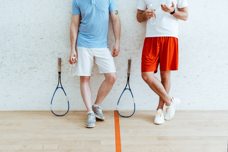 Cropped view of two squash players in shorts standing with crossed legs in four-walled courtの写真素材