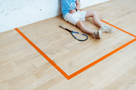 Cropped view of squash player sitting on floor and holding bottle of waterの写真素材