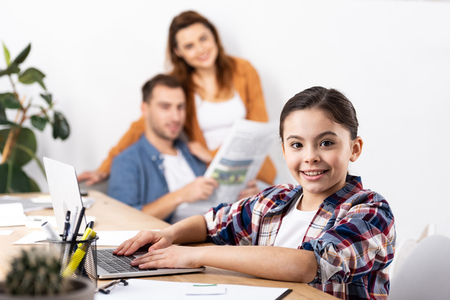 Selective focus of cheerful kid with laptop near parents at homeの写真素材