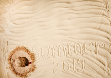 Top view of summer 2019 written on wavy sand with straw hat and copy spaceの写真素材