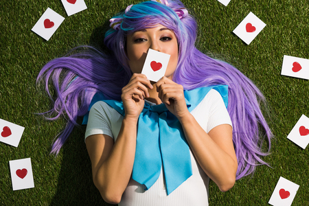 Asian anime girl in purple wig holding card and lying on grassの写真素材