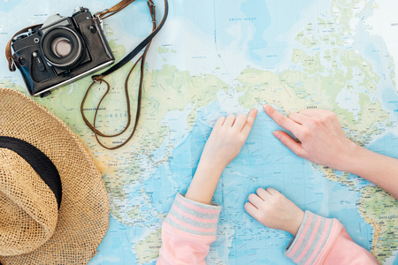 Cropped view of child and woman with straw hat and film camera pointing with fingers on world mapの写真素材
