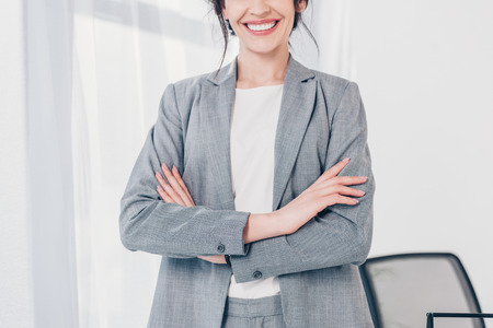 Cropped view of smiling businesswoman in suit with crossed arms in officeの写真素材