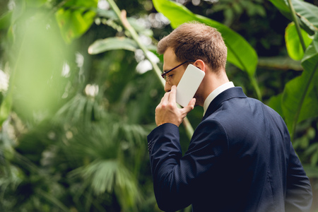 Businessman in suit and glasses talking on smartphone in greenhouseの写真素材