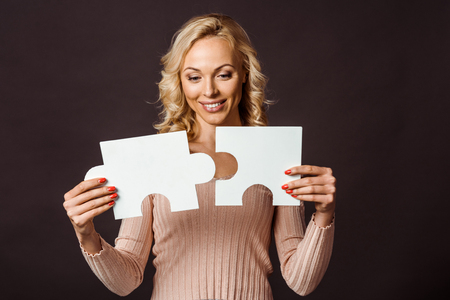 happy blonde woman connecting jigsaw pieces isolated on blackの写真素材